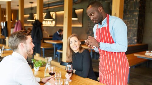 Black man serving a man and a woman in restaurant