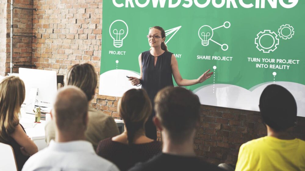 An instructor stands in front of a board to discuss crowdsourcing with graphics.