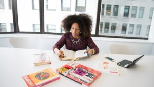 A woman of color works at her desk taking notes on a project.