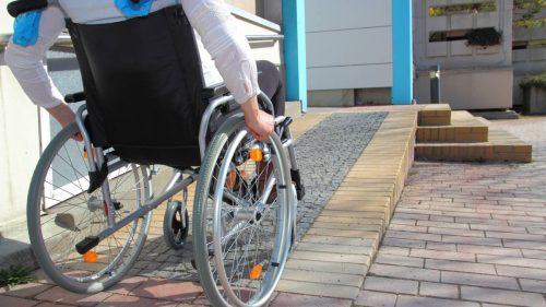 A person in a wheelchair ascends a ramp to enter a building as an example of accessibility.