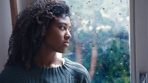 Depressed Black woman looking outside a rainy window