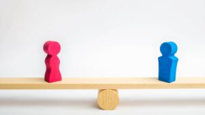Two people figures stand in balance on a see saw to demonstrate fairness. The article covers workplace fairness specifically.